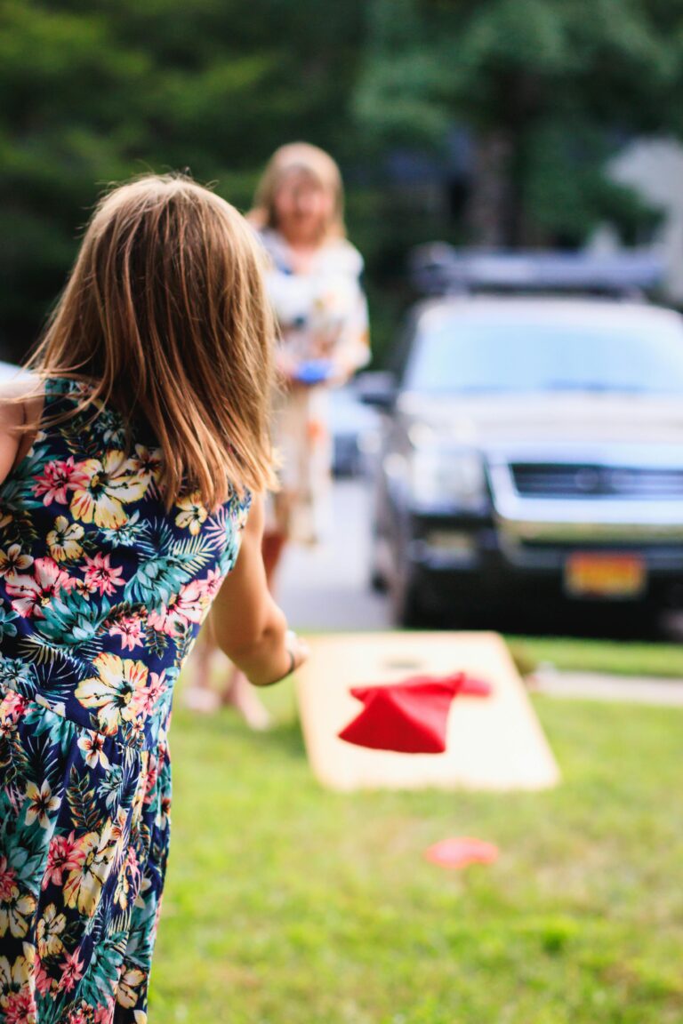 Two young girls enjoy a game of cornhole in a sunny park setting.