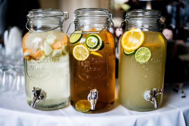 Close-up of citrus-infused drinks in stylish glass jars with tap dispensers, perfect for summer refreshment.